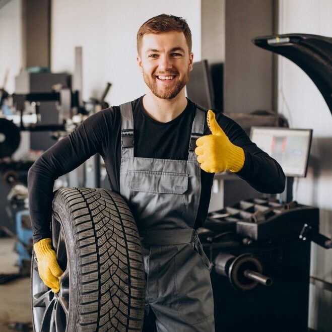 car mechanic wearing black uniform holding a tyre in the garage