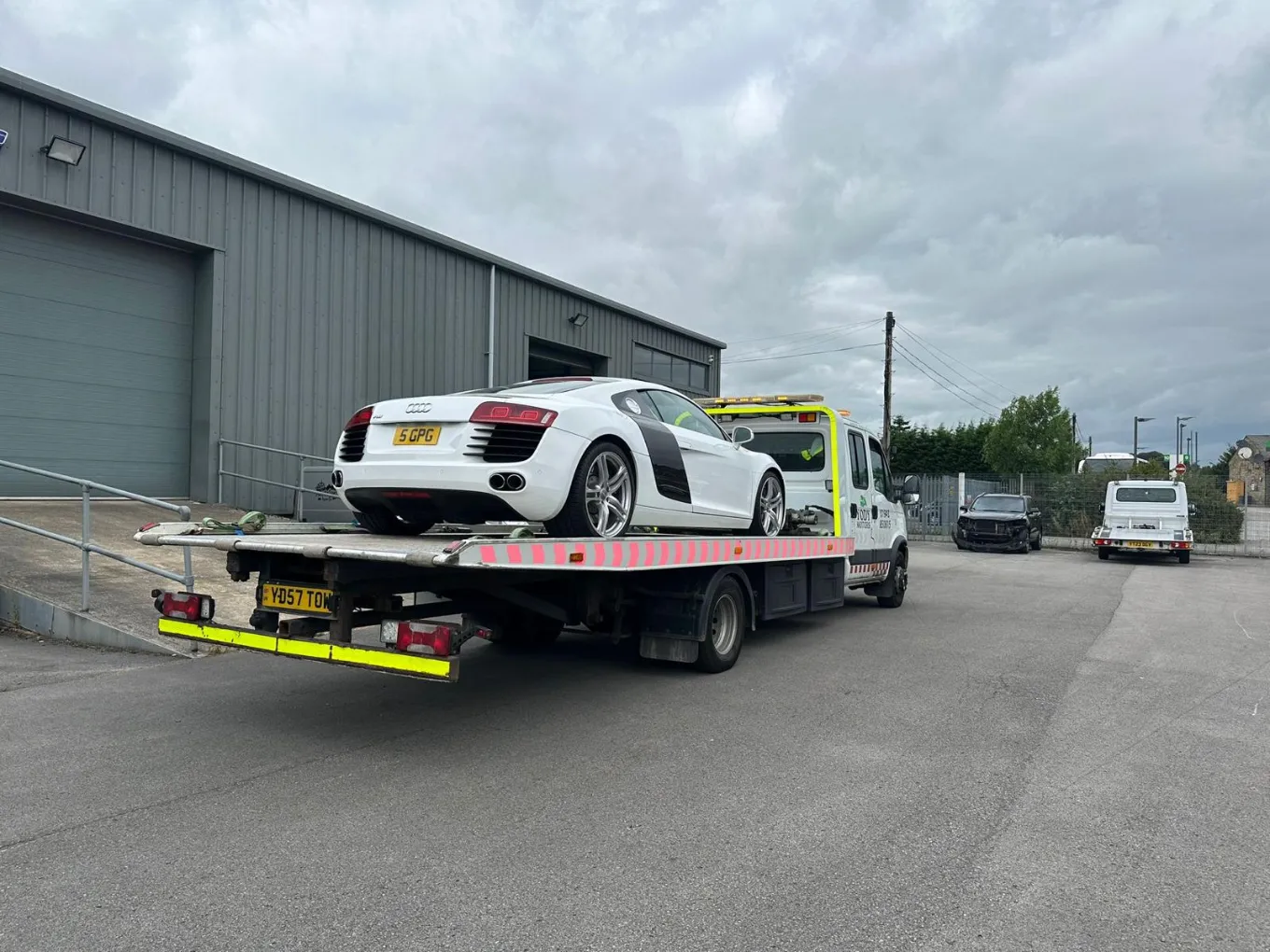 white Audi R8 being transported on a flatbed tow truck